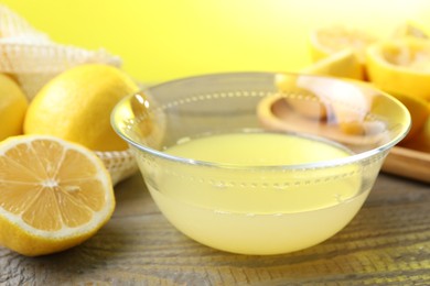 Bowl with fresh lemon juice and fruits on wooden table, closeup