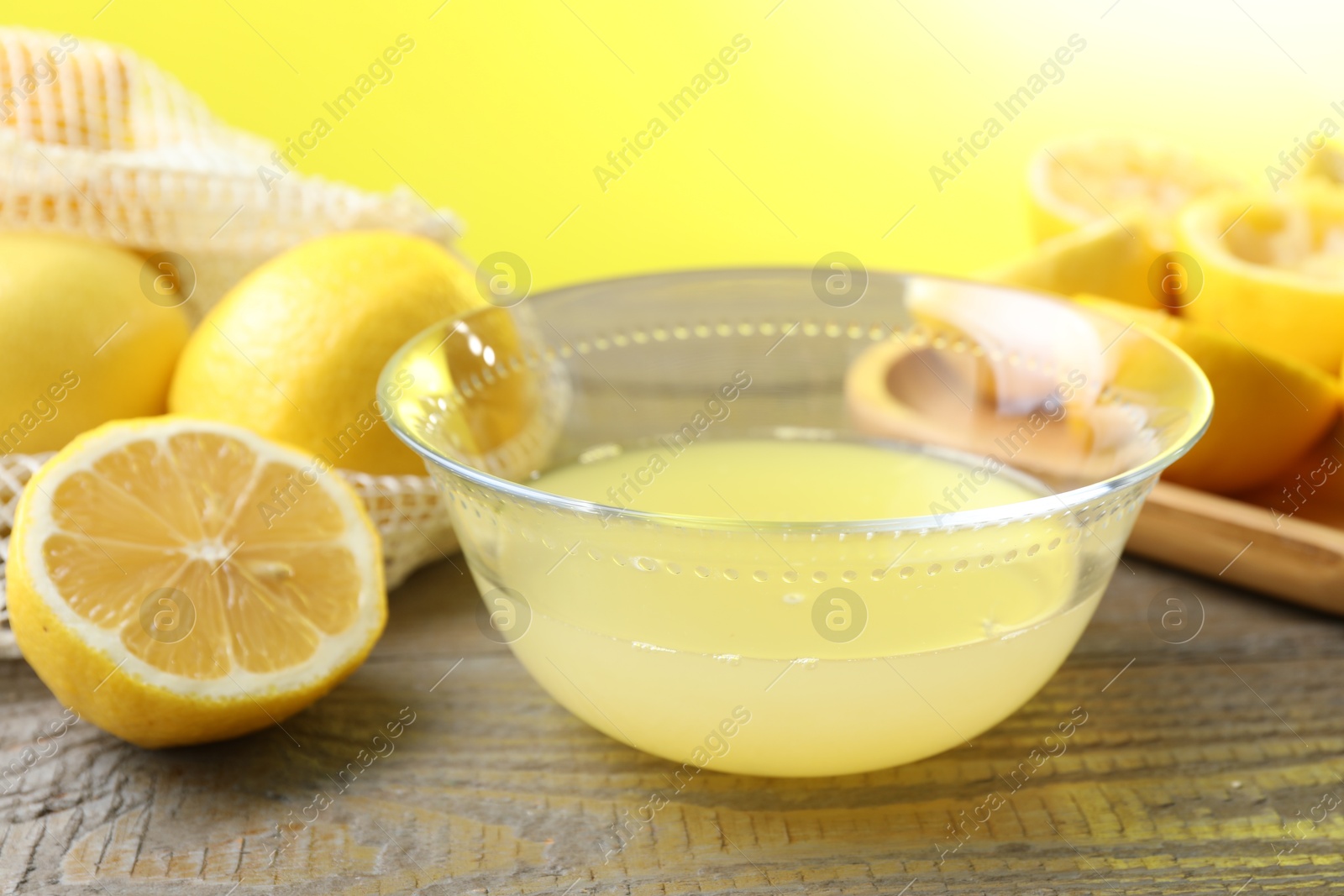 Photo of Bowl with fresh lemon juice and fruits on wooden table, closeup