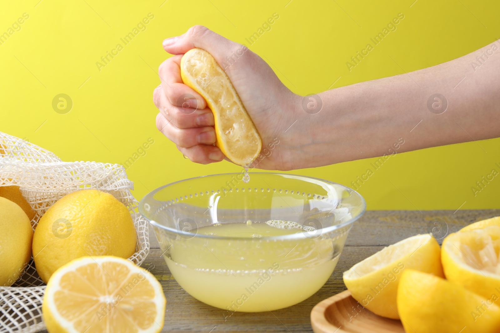 Photo of Woman squeezing lemon juice into bowl at wooden table, closeup