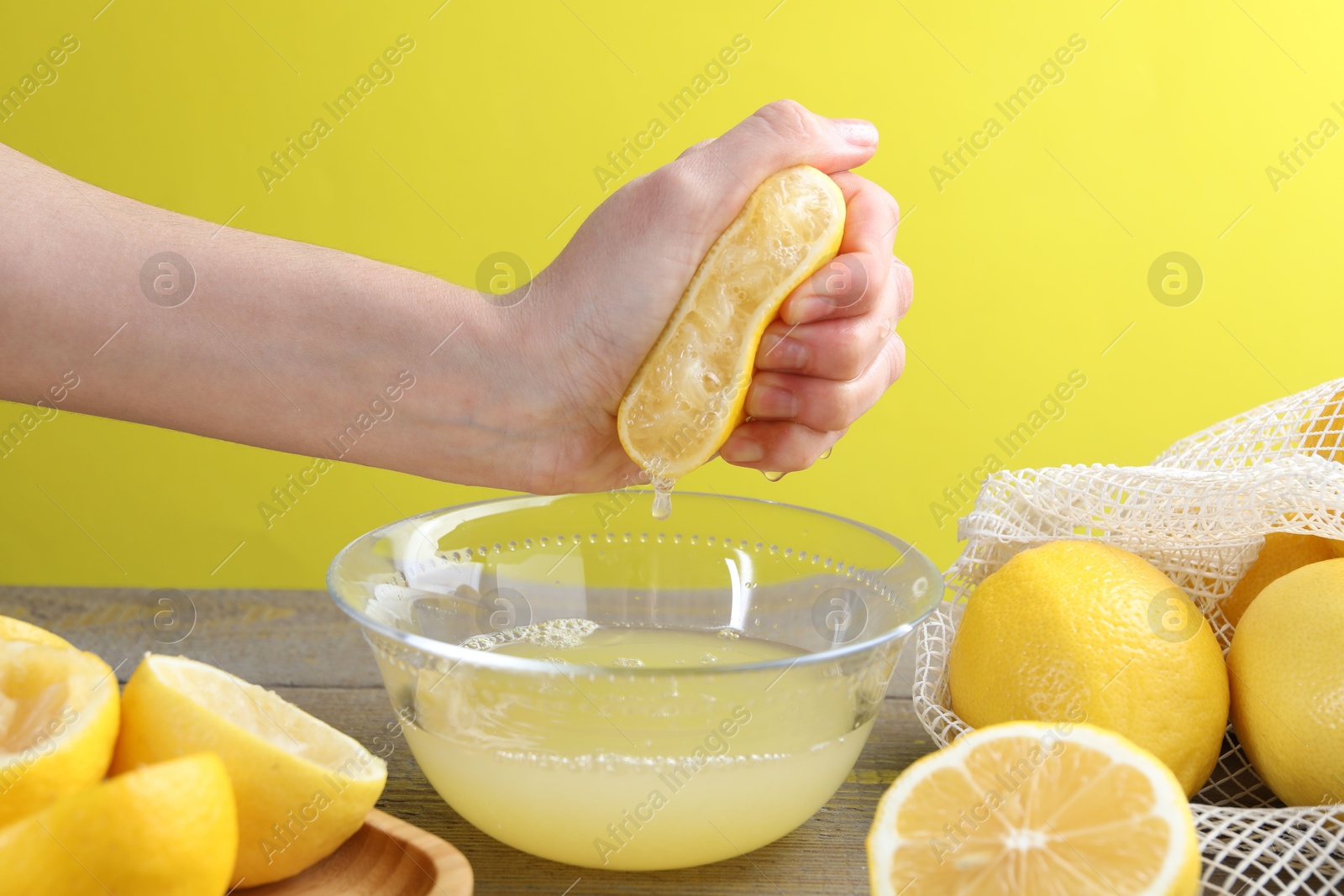 Photo of Woman squeezing lemon juice into bowl at wooden table, closeup