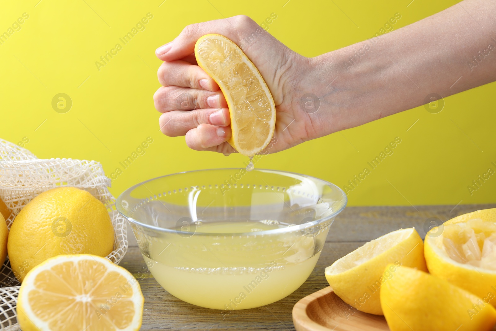 Photo of Woman squeezing lemon juice into bowl at wooden table, closeup