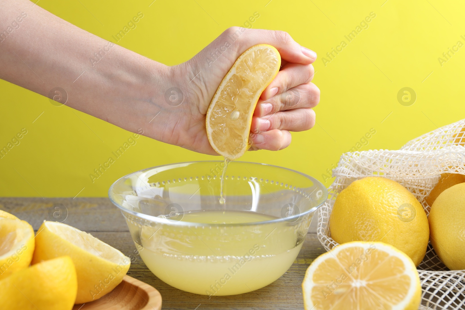 Photo of Woman squeezing lemon juice into bowl at wooden table, closeup