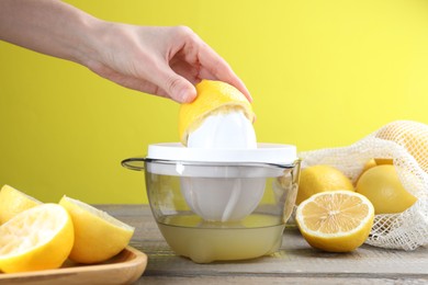 Photo of Woman with lemon using juicer at wooden table, closeup