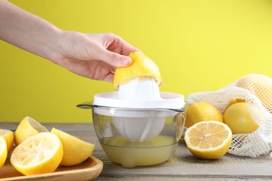 Photo of Woman with lemon using juicer at wooden table, closeup