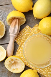 Bowl with fresh lemon juice, squeezer and fruits on wooden table, flat lay