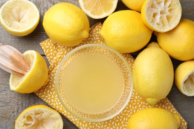 Photo of Bowl with fresh lemon juice, squeezer and fruits on wooden table, flat lay