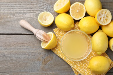 Photo of Bowl with fresh lemon juice, squeezer and fruits on wooden table, flat lay