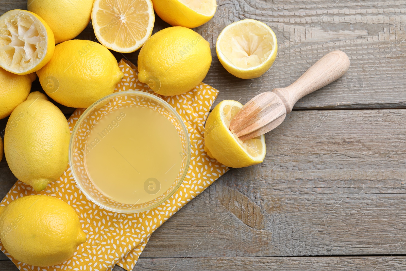 Photo of Bowl with fresh lemon juice, squeezer and fruits on wooden table, flat lay