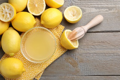 Bowl with fresh lemon juice, squeezer and fruits on wooden table, flat lay