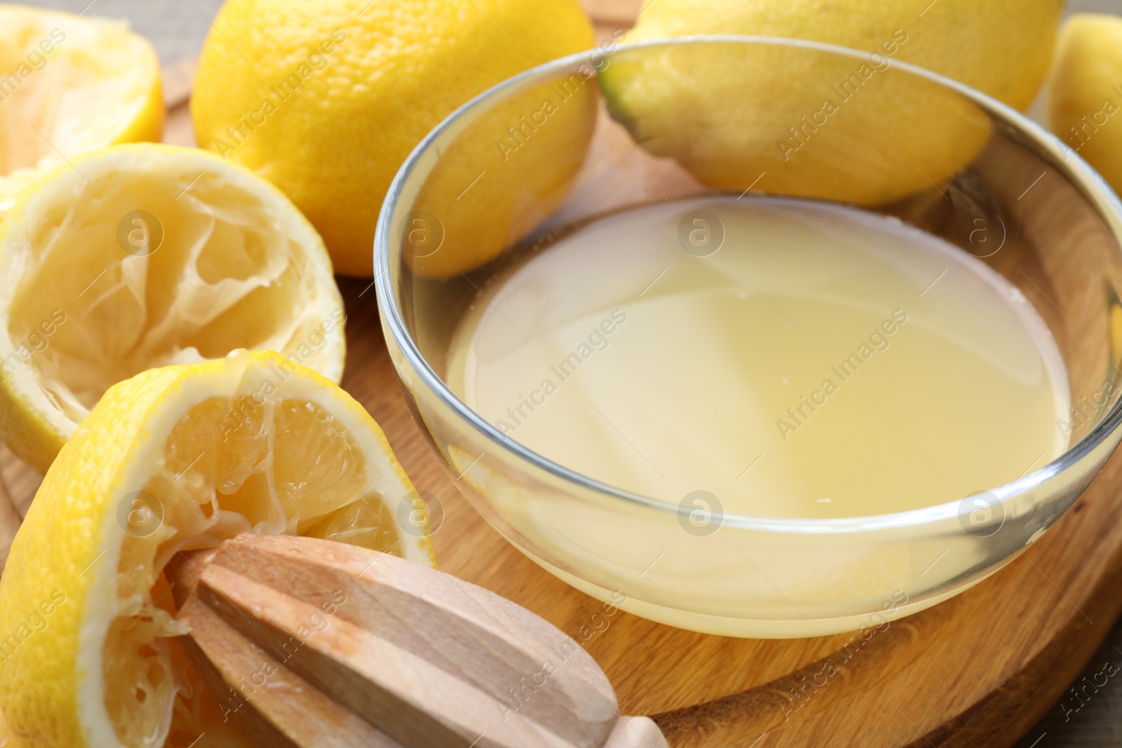 Photo of Bowl with fresh lemon juice, squeezer and fruits on wooden table, closeup