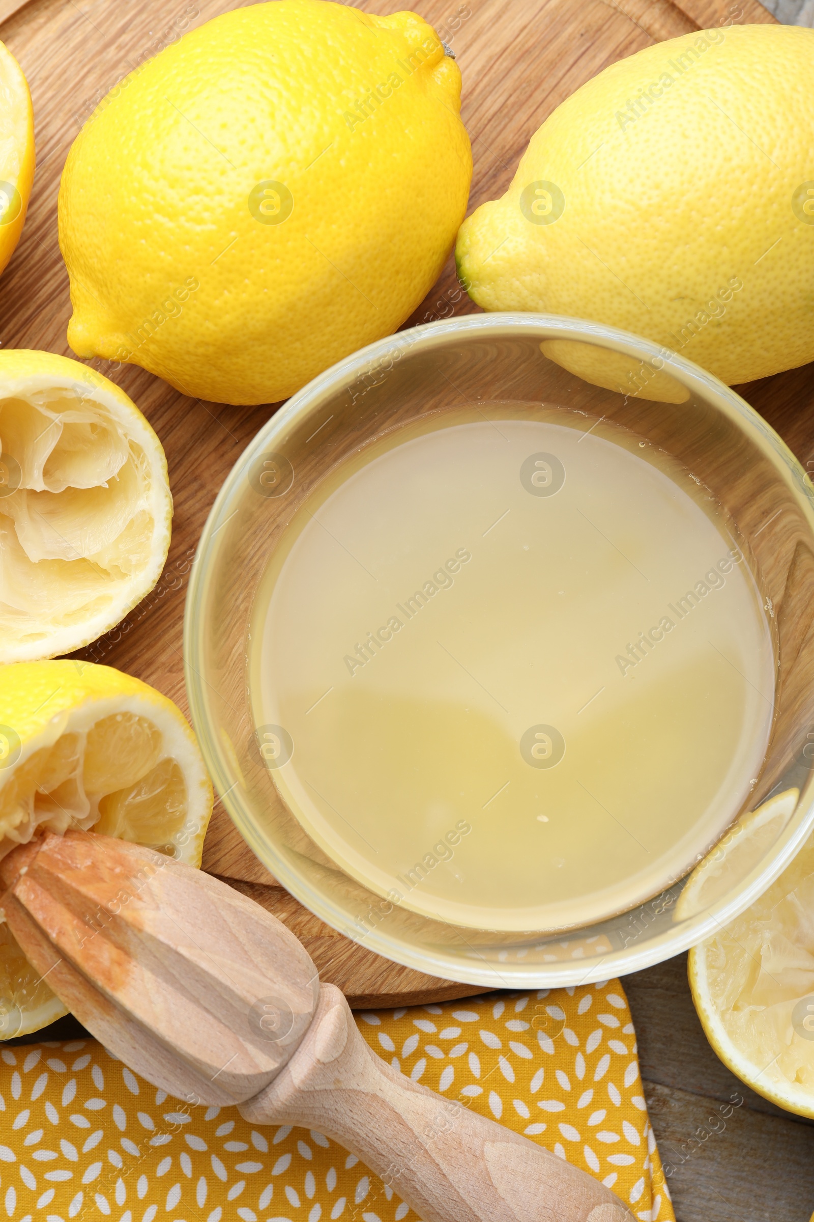 Photo of Bowl with fresh lemon juice, squeezer and fruits on wooden table, flat lay