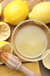 Photo of Bowl with fresh lemon juice, squeezer and fruits on wooden table, flat lay