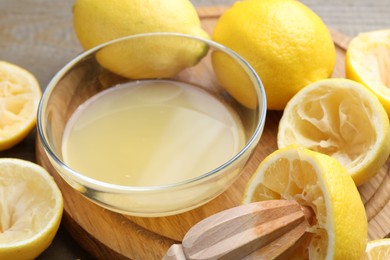 Photo of Bowl with fresh lemon juice, squeezer and fruits on wooden table, closeup