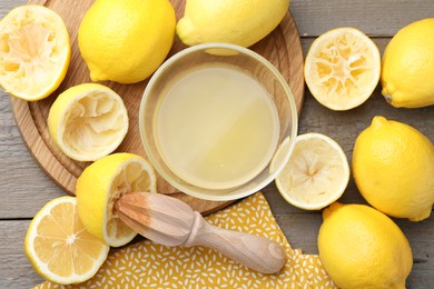 Photo of Bowl with fresh lemon juice, squeezer and fruits on wooden table, flat lay