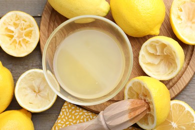 Photo of Bowl with fresh lemon juice, squeezer and fruits on wooden table, flat lay