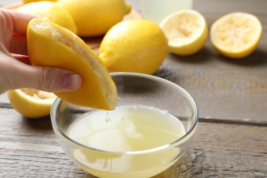 Photo of Woman squeezing lemon juice into bowl at wooden table, closeup