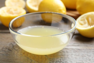 Photo of Bowl with fresh lemon juice and fruits on wooden table, closeup