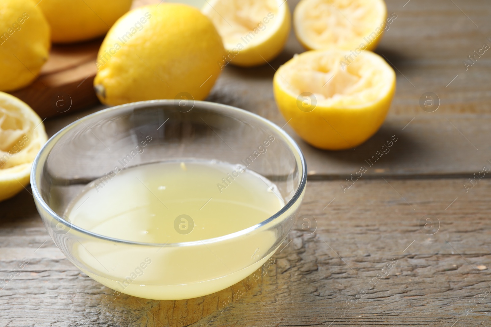 Photo of Bowl with fresh lemon juice and fruits on wooden table, closeup