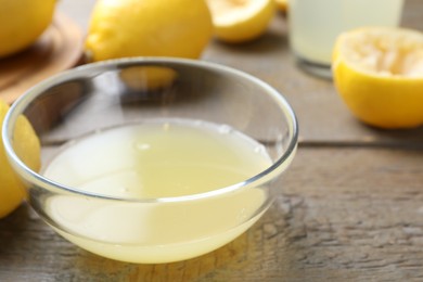 Photo of Bowl with fresh lemon juice and fruits on wooden table, closeup