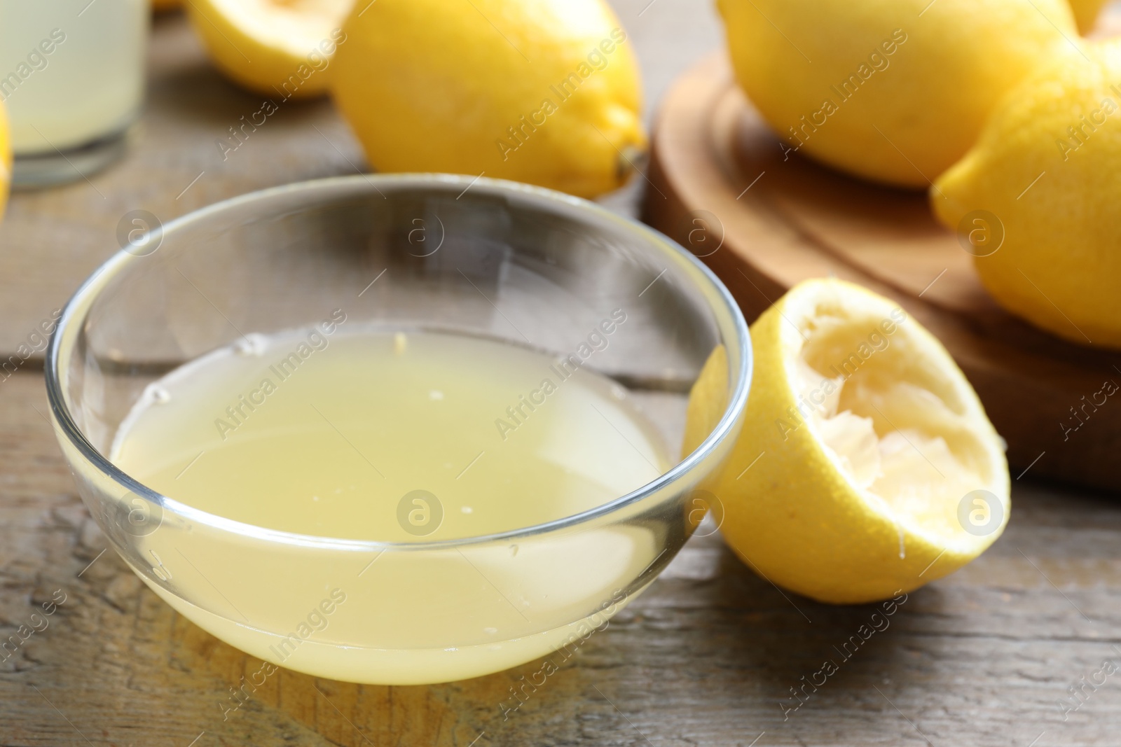 Photo of Bowl with fresh lemon juice and fruits on wooden table, closeup