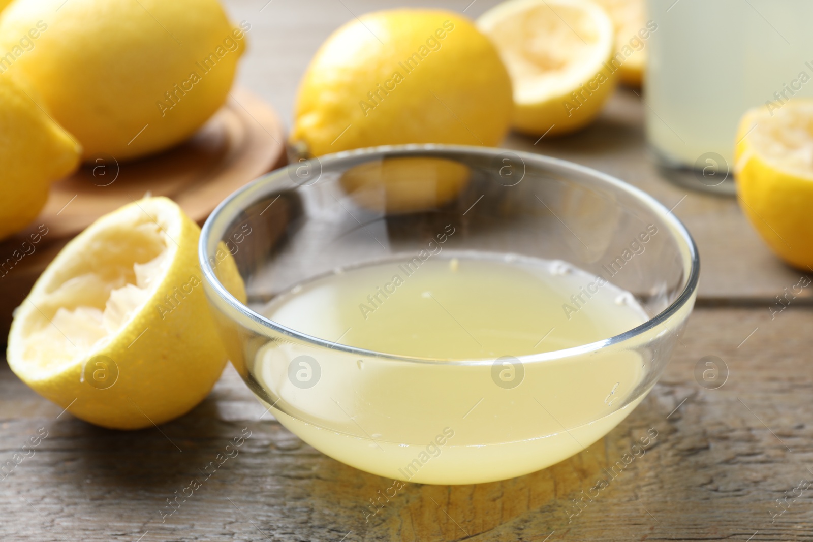 Photo of Bowl with fresh lemon juice and fruits on wooden table, closeup