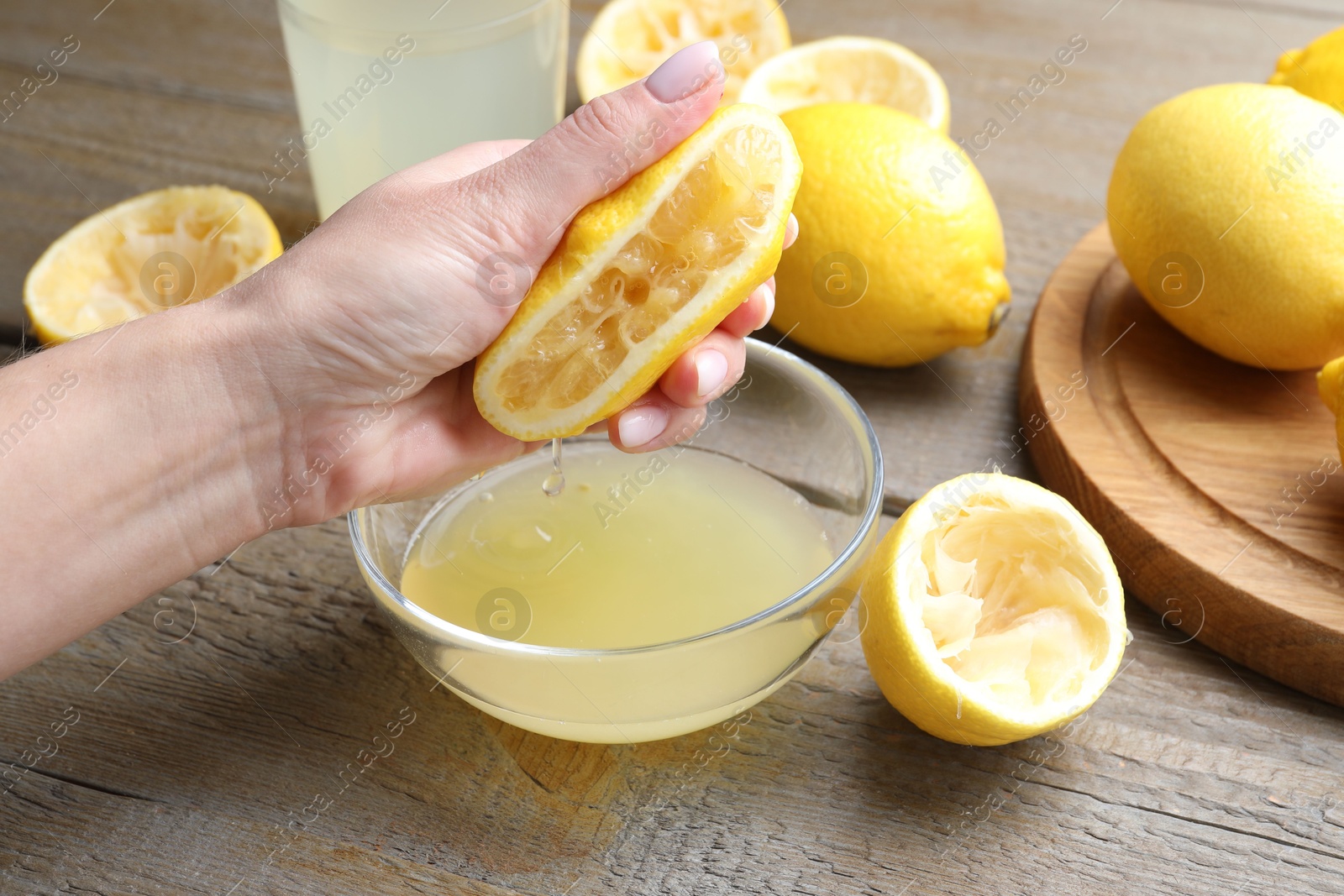 Photo of Woman squeezing lemon juice into bowl at wooden table, closeup