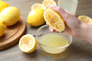 Photo of Woman squeezing lemon juice into bowl at wooden table, closeup