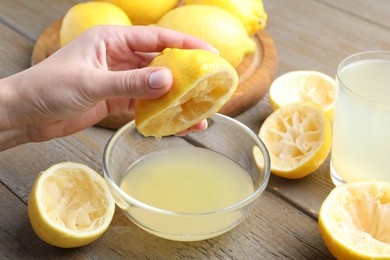 Photo of Woman squeezing lemon juice into bowl at wooden table, closeup