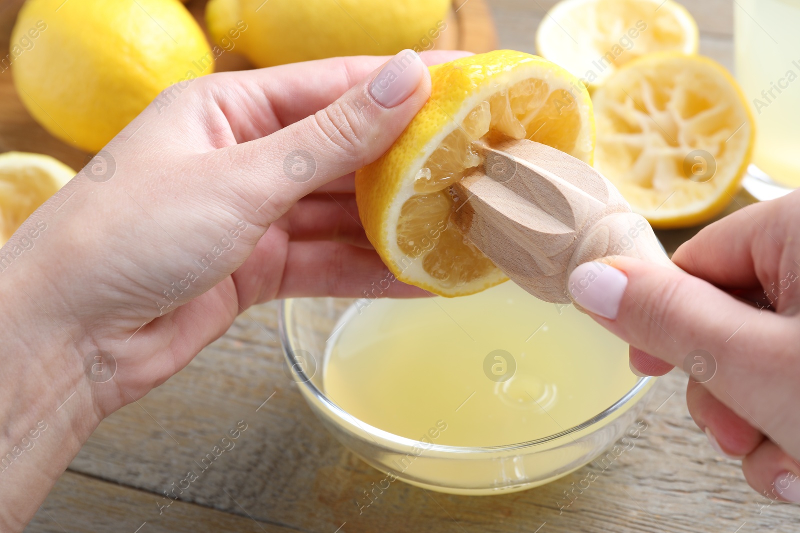 Photo of Woman juicing lemon into bowl at wooden table, closeup