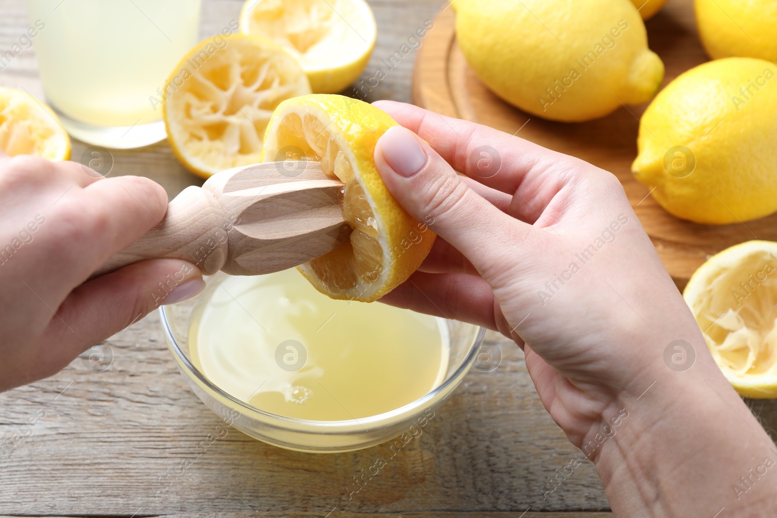 Photo of Woman juicing lemon into bowl at wooden table, closeup