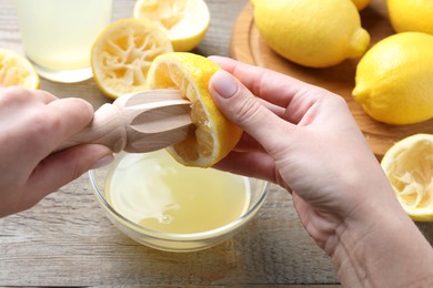 Woman juicing lemon into bowl at wooden table, closeup