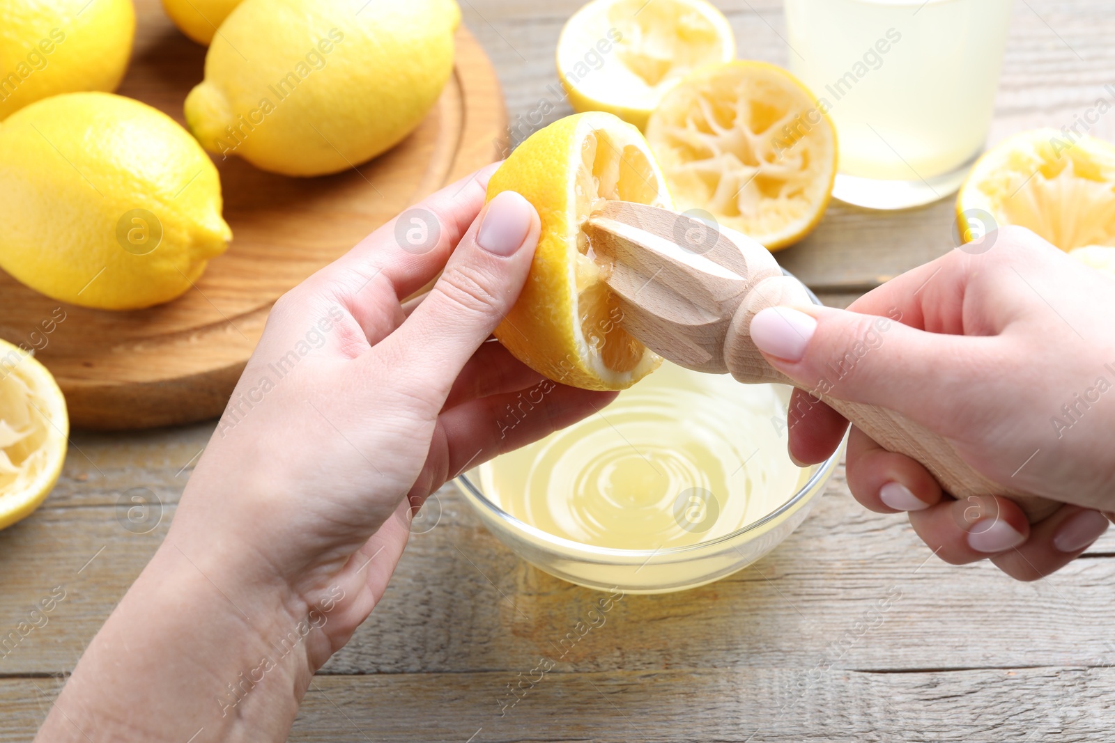 Photo of Woman juicing lemon into bowl at wooden table, closeup