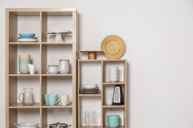 Photo of Wooden shelving units with kitchenware near white wall indoors