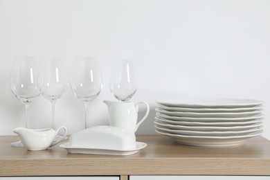 Photo of Tableware on wooden storage cabinet near white wall indoors