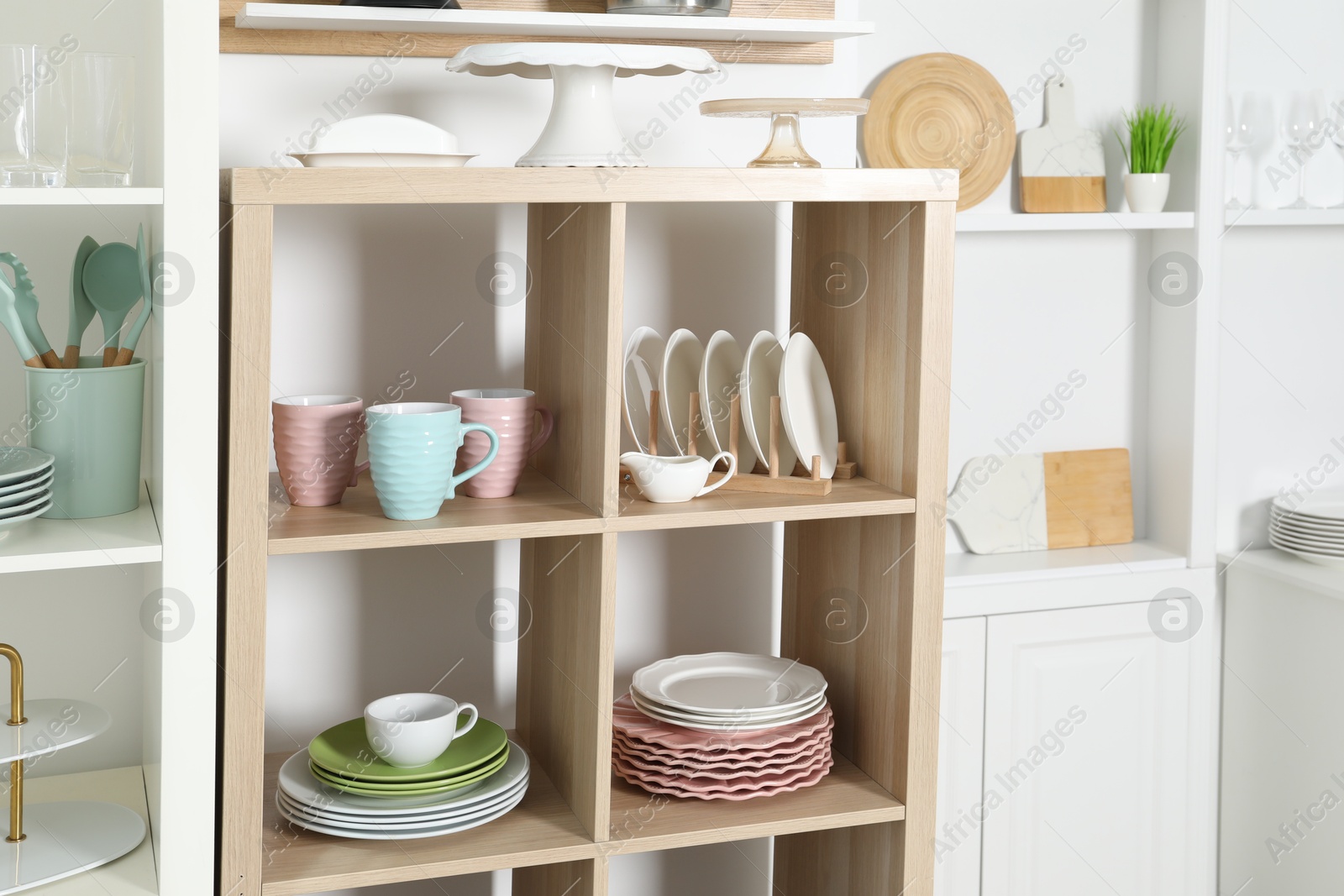 Photo of Shelving units with kitchenware near white wall indoors