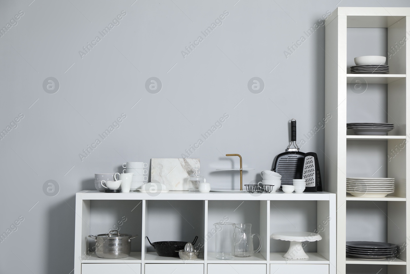 Photo of Shelving unit and storage cabinet with kitchenware near grey wall indoors