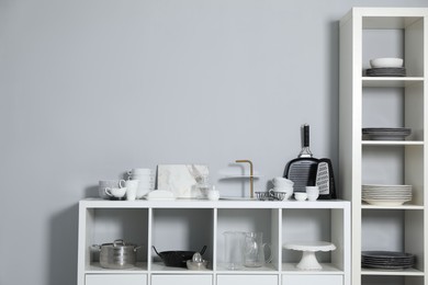 Photo of Shelving unit and storage cabinet with kitchenware near grey wall indoors