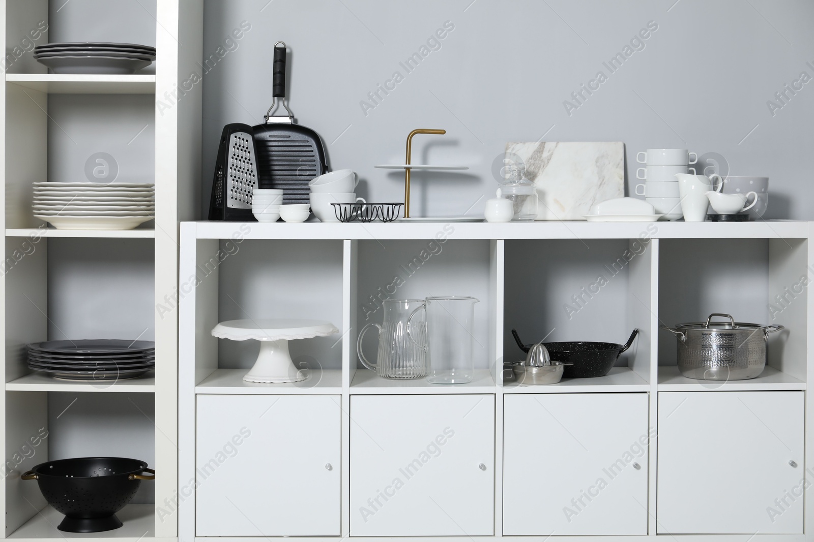 Photo of Shelving unit and storage cabinet with kitchenware near grey wall indoors