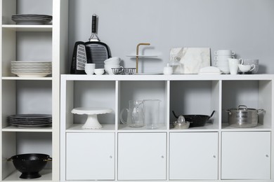 Shelving unit and storage cabinet with kitchenware near grey wall indoors