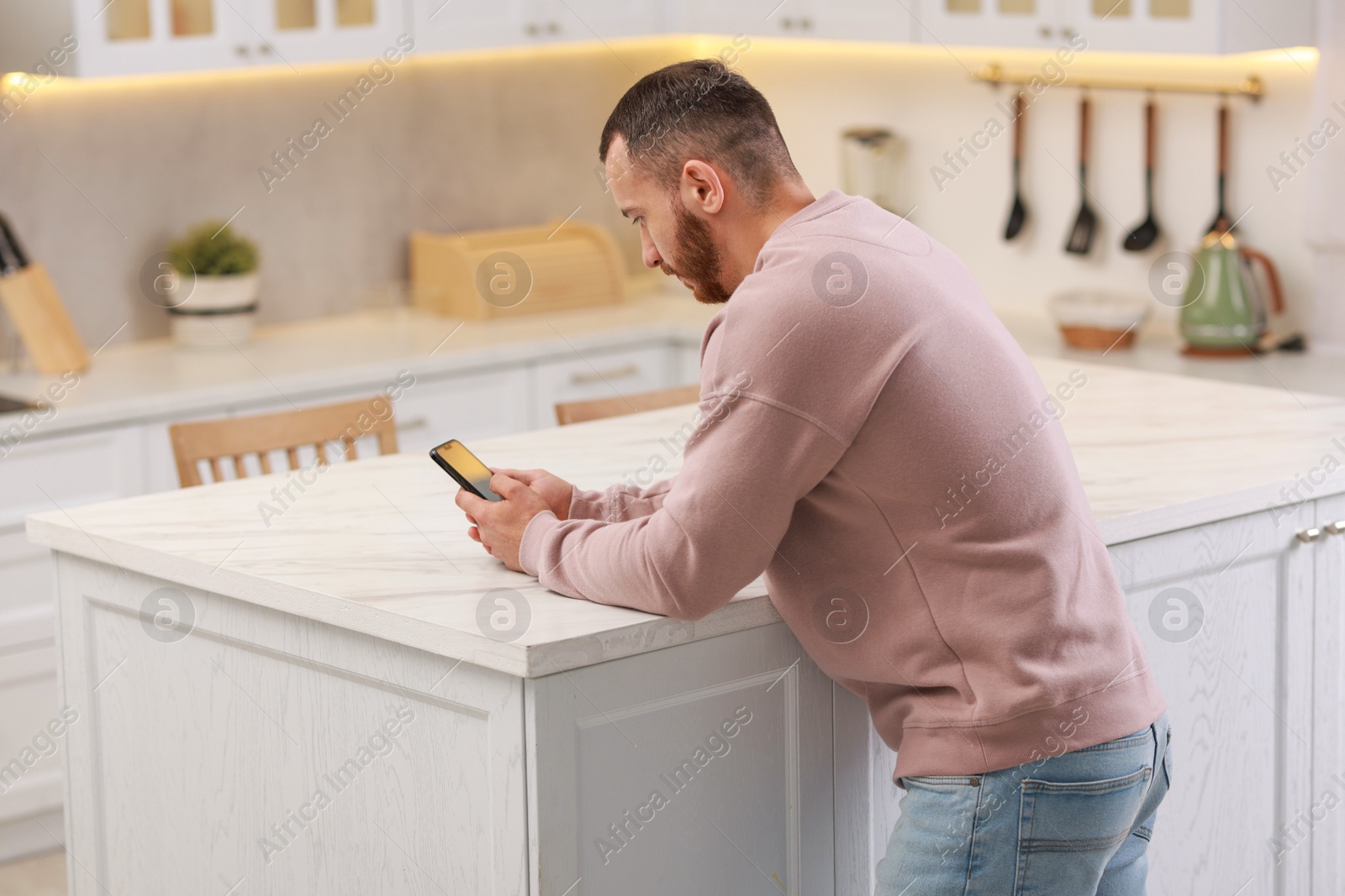 Photo of Handsome man looking at smartphone in kitchen