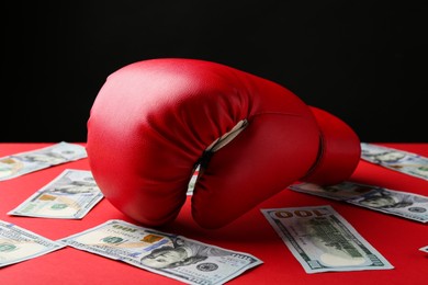 Photo of Boxing glove and dollar banknotes on red table