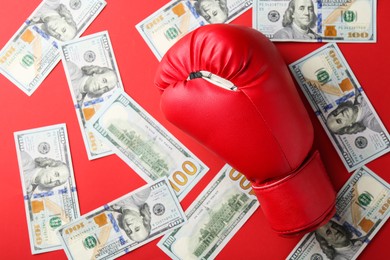 Photo of Boxing glove and dollar banknotes on red background, top view