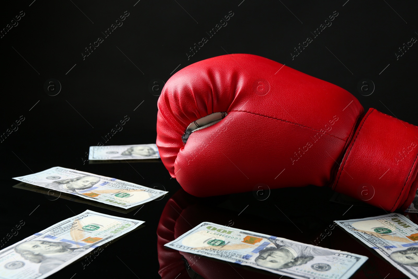 Photo of Red boxing glove and dollar banknotes on black mirror surface