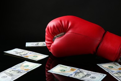 Photo of Red boxing glove and dollar banknotes on black mirror surface