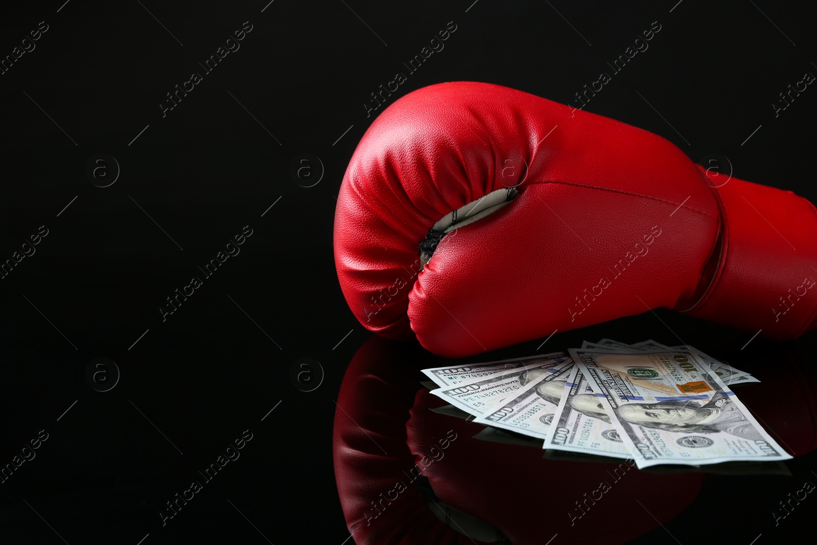 Photo of Red boxing glove and dollar banknotes on black mirror surface, space for text