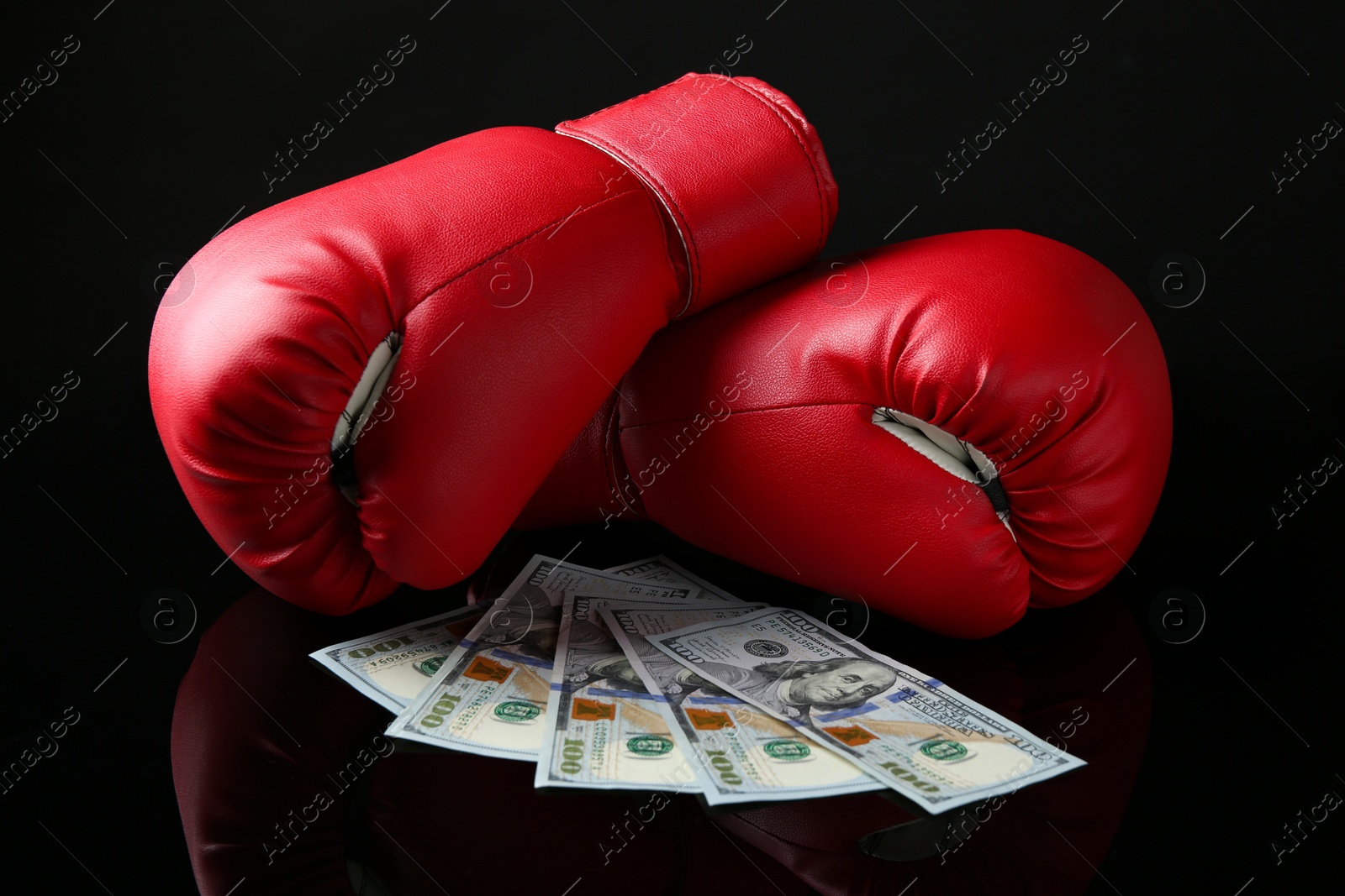 Photo of Pair of red boxing gloves and dollar banknotes on black mirror surface