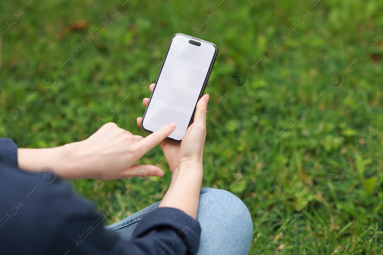 Photo of Woman using smartphone on green grass outdoors, closeup