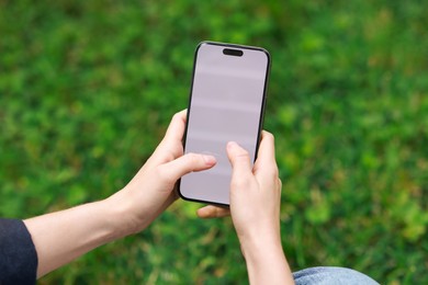 Photo of Woman using smartphone on green grass outdoors, closeup