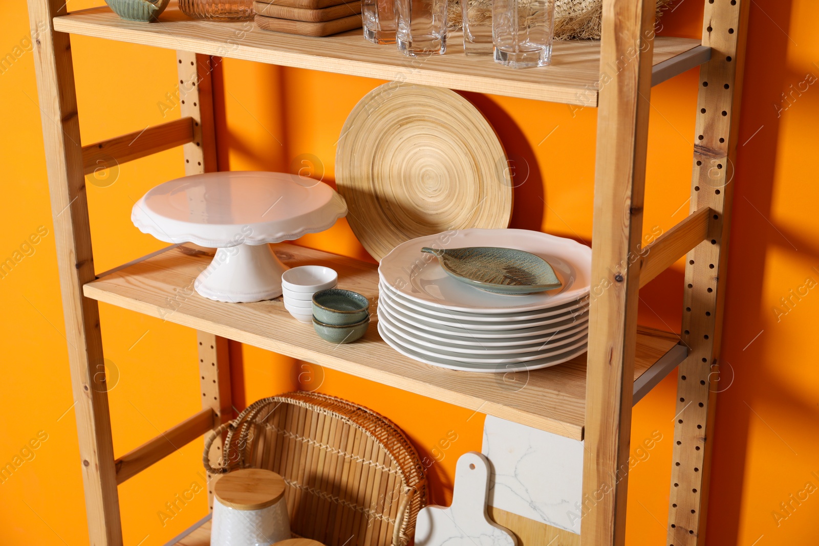 Photo of Wooden storage stand with kitchenware near orange wall indoors