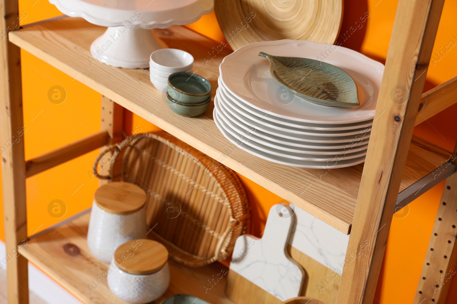 Photo of Wooden storage stand with kitchenware near orange wall indoors, closeup